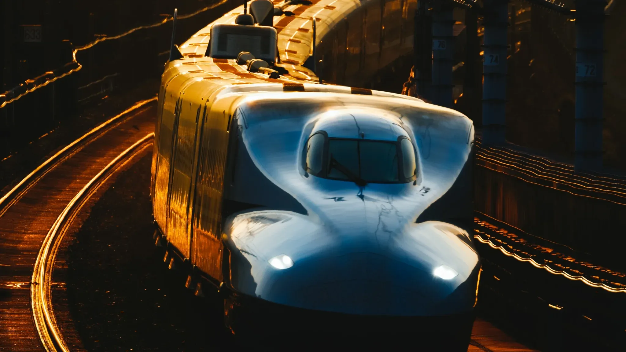 A Shinkansen bullet train with a rounded nose gliding along curved tracks in warm golden light.